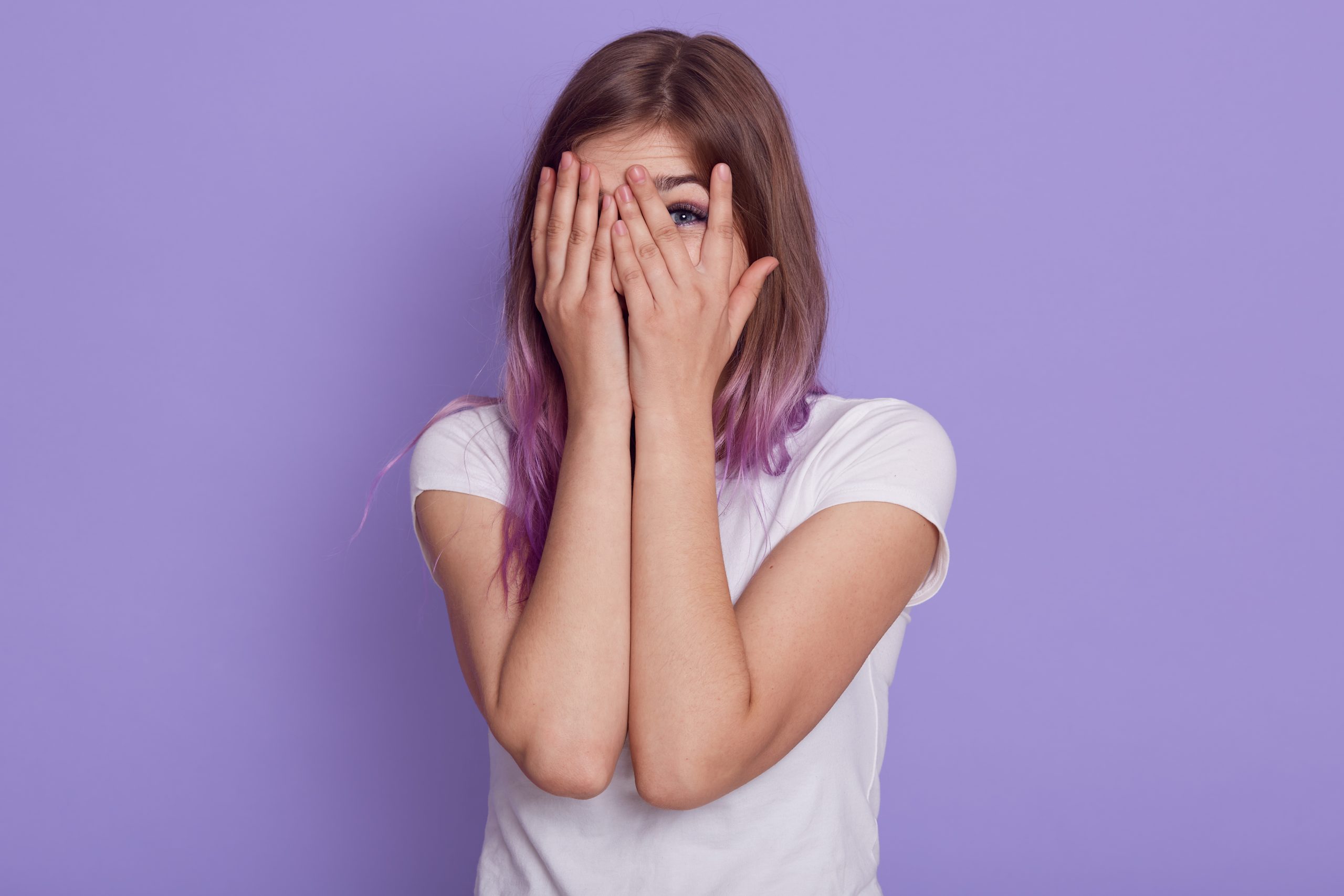 attractive-young-woman-wearing-white-casual-t-shirt-covering-her-face-with-palms-looking-through-fingers-spying-somebody-isolated-purple-wall-scaled